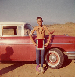 Loinclothed hobby; Obrzek dne - the picture od the day - awa rel -  Skinny boy in indian dance costume on red car in desert - 1950